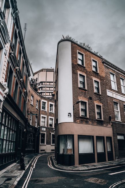 A narrow cobbled street in an urban residential area with closely packed multi-storey buildings on either side. The buildings are constructed with brick and stone, featuring various styles of windows,