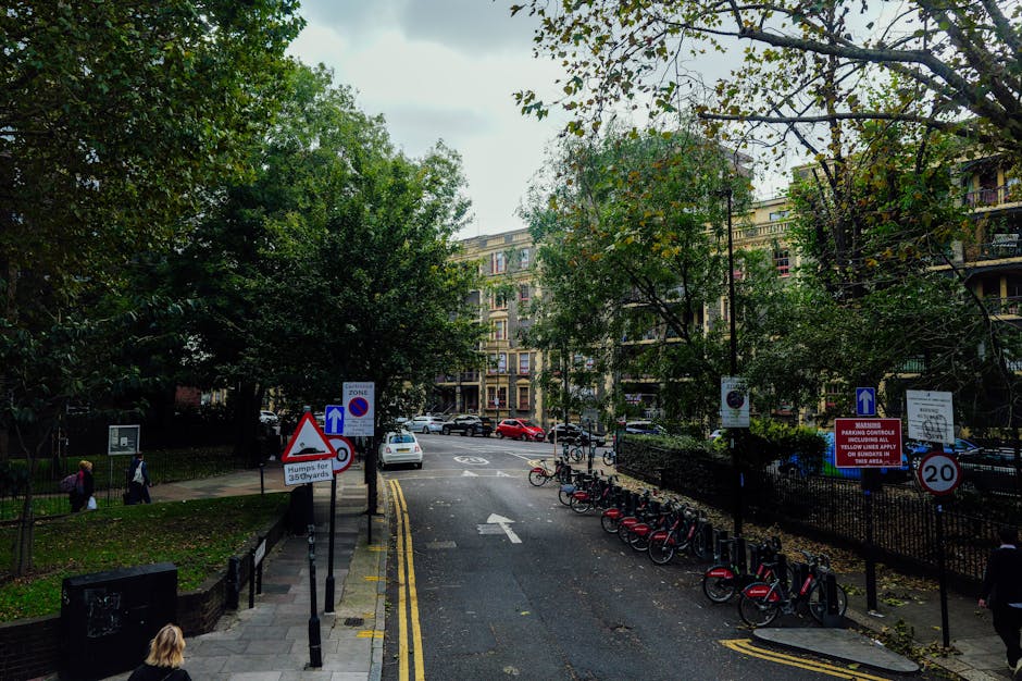 A city street scene in London featuring a white delivery van parked outside multi-storey buildings with architectural details typical of a home relocation environment. The buildings include brick faca