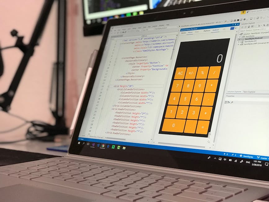 A close-up view of a laptop computer placed on a desk, displaying a code editor with lines of programming code in various colours and a calculator application with orange buttons for basic arithmetic 